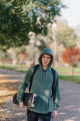 Teenage man walking carrying a skateboard in park