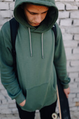 Teenage boy standing, looking down, holding skateboard