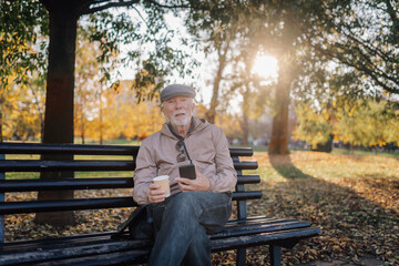 Senior man relaxing in park with smartphone and coffee