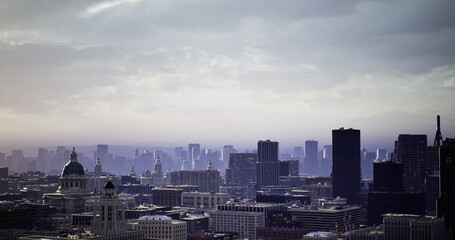 Fototapeta premium hazy skyline with layered silhouettes of towers and rooftops, soft morning light filtering through cloud cover, mood of quiet industry and contemplative urban