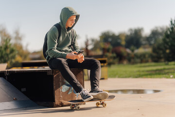 Teenager sitting on skateboard checking phone in skatepark