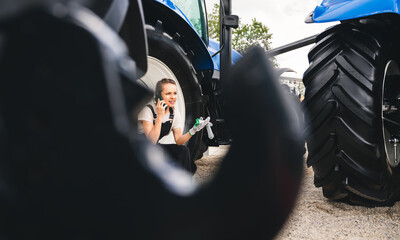 Female farmer sits on the wheel of tractor and talks on phone. © Barillo Images