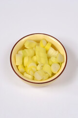 A top view of a small yellow ceramic bowl filled with freshly chopped spring onions isolated on a plain white background