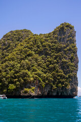 Naklejka premium A massive, rounded limestone karst formation towering over turquoise waters. The cliff is almost entirely covered in thick, dark green tropical forest. Exotic and tropical landscape.
