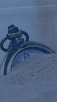 Vertical video: Falling sand stream starting, antique pocket watch slowly burying, showing time