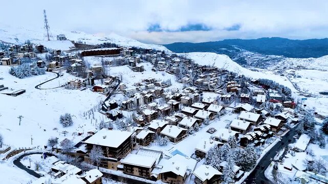 Drone Aerial shot of Kfardebian village blanketed in snow with mountain backdrop. Winter tourism destination featuring chalets, hotels and alpine landscape in Lebanon.
