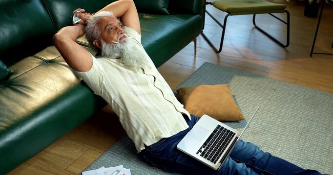 Indian mid age bearded man counting cash Indian rupees and relaxing between work sitting on carpet in modern home, stylish mature male managing household finance and budget indoors