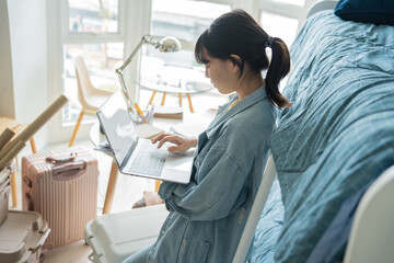 Obraz premium Student asian woman sitting on bed in dorm room college student&nbsp;Work or homework on laptop in university dormitory