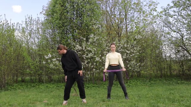 A young couple exercising outdoors in the summer, using a barbell and elastic band