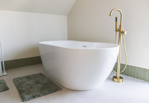 Modern Freestanding Bathtub with Gold Fixtures in a Minimalist Attic Bathroom