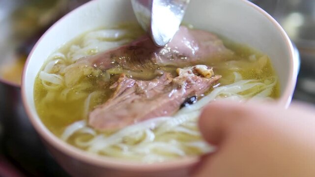 Authentic Vietnamese pho bo soup preparation process with pouring rich broth over rice noodles adding fresh herbs and assembling traditional ingredients in a flavorful culinary scene