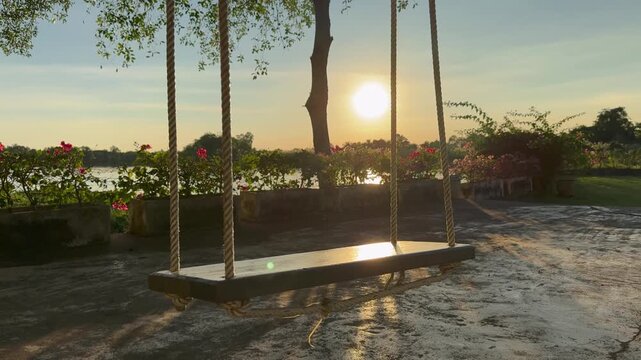 An empty swing sways gently by the river as the sun sets.