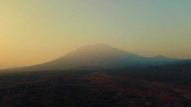 A stunning sunrise over Mount Batur and Mount Agung in Bali reveals mist-covered settlements and lush green plantations. The early light casts a serene glow over the breathtaking landscape.