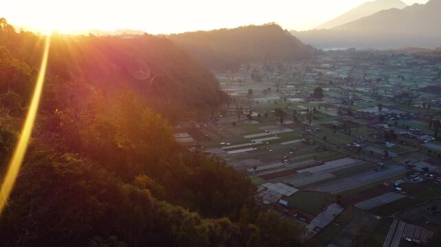 A stunning sunrise over Mount Batur and Mount Agung in Bali reveals mist-covered settlements and lush green plantations. The early light casts a serene glow over the breathtaking landscape.