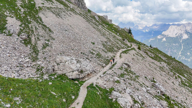 Aerial, bird view, hiking trail with some hikers, tourists along a mountain slope with grass and rocks,  near Rotwandh&uuml;tte, Rifugio Roda di Va&egrave;l mountain hut in Italian Dolomites. Beautiful hiking des