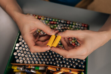 Top view of person holding two yellow aa batteries, preparing them for responsible recycling and...