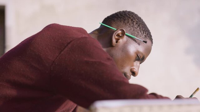 Black man executing fine brushwork on surface, intense closeup profile, pencil tucked behind ear, studio light catching textured pigment, steady hand guiding precise strokes, focused emotional