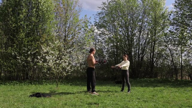 A young couple exercising outdoors in the summer, using a barbell and elastic band