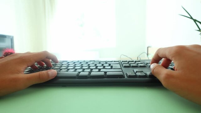 Close up side view of hands typing on a black keyboard over a mint green mat, soft window light, blurred cactus in background, evoking focused work, digital fluency, and calm productivity.