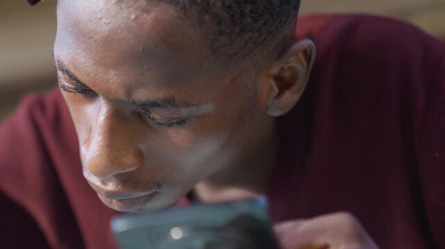 Closeup black painter examining phone, face flecked with white paint, burgundy sweater, indoor workshop, focused expression, soft natural light, contemplative mood, inspecting reference image, quiet