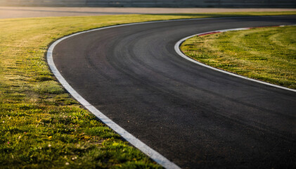 Obraz premium Clean asphalt race track curve with white line marking and green grassy runoff area on a bright, sunny day, ready for speed and competition