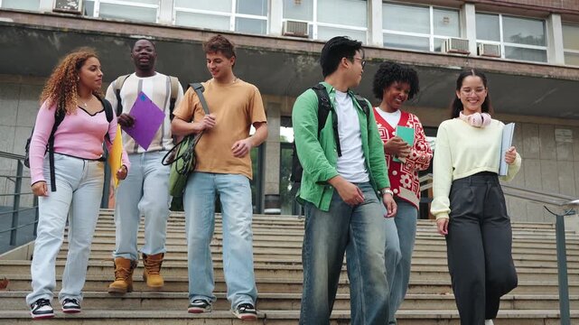 Happy international university classmate friends walking together in stairway campus, talking and laughing outdoors after school