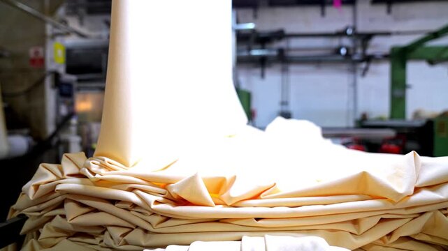 Professional industrial footage reflecting manufacturing discipline and quality standards. Processed fabric descending from machinery and neatly stacked in a textile factory.
