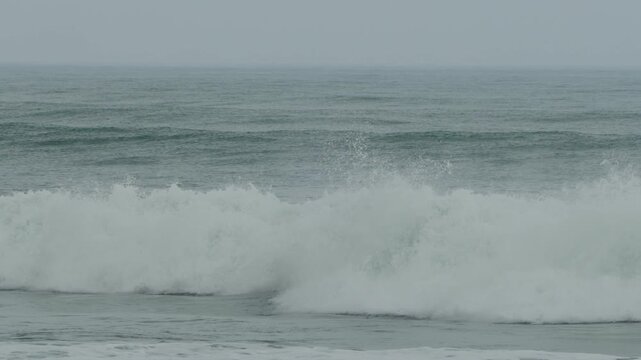 Slow panning following view of a strong wave in slow motion  as it is passing through the coastline of tropical beach during the heavy windy monsoon season.