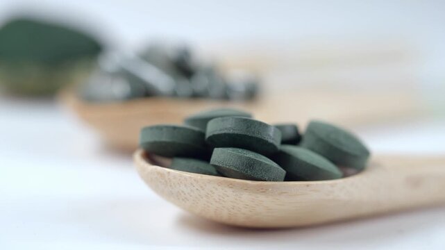 Spirulina tablets in wooden spoon showing organic superfood supplement details for healthy lifestyle and wellness