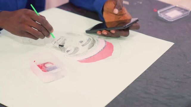 Black artist painting portrait with phone, mobile reference and wider studio view, hand holding phone while brush adds gray tones and pink wash, plastic paint tray, freelance commission vibe, modern