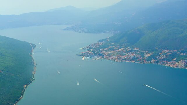 Aerial view from airplane window while takeoff from Tivat, view of city and Kotor Bay, Montenegro. Mediterranean coast with turquoise Adriatic Sea, sandy beaches, green mountains and summer clouds ove