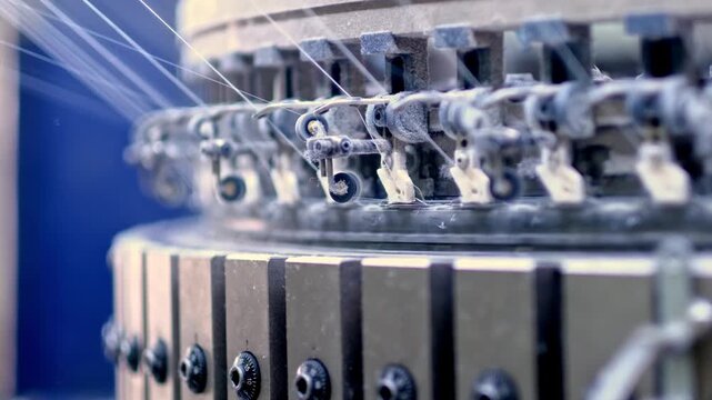 Professional industrial footage reflecting automation and precision manufacturing. Detailed view of needle and yarn mechanism on a high speed knitting machine.