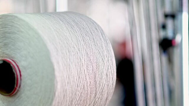 Professional industrial footage reflecting textile manufacturing process and infrastructure. Thread spools aligned on racks inside a textile factory production area.