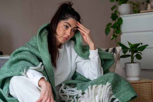 Beautiful young sad woman sitting at home wrapped in a blanket