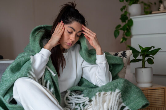 Beautiful young sad woman sitting at home wrapped in a blanket