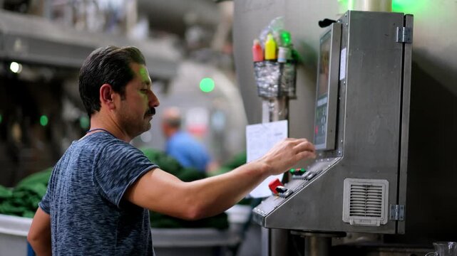 Professional industrial footage reflecting human labor, work discipline and technical responsibility. Worker operating a control panel on a textile production line.