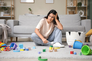 Tired young mother resting among scattered children's toys at home. Stress concept