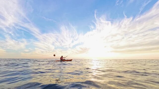 Kayak sunset ocean featuring a man rowing his small boat toward a coastal cliff during golden hour for summer adventure