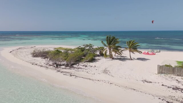 Aerial drone view of a kite surfer riding across crystal-clear turquoise water near a white sand tropical beach lined with palm trees in Caribbean paradise, Antigua and Barbuda