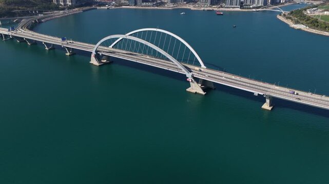 tunning aerial drone perspective of the Tseung Kwan O Cross Bay Link Bridge in Hong Kong, showcasing modern architecture, coastal transport infrastructure, and urban connectivity on a clear sunny day.