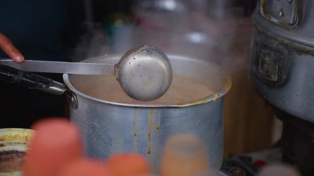 Street seller stirring hot steaming Masala chai tea in steel pots with ladle in Nainital India