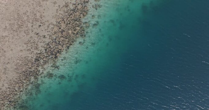 Top-down drone view of coral reef meeting deep blue ocean in West Bali National Park, Indonesia. Turquoise shallows, exposed reef and clear tropical water forming natural coastal patterns