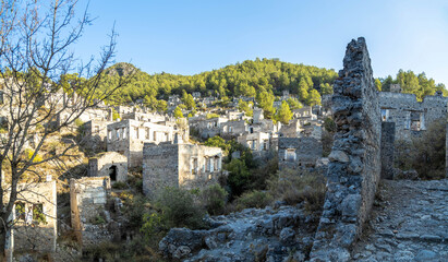 Fototapeta premium Panoramic view of Kayakoy ghost town with abandoned stone houses. Ancient ruins of a greek village on a green hill near Fethiye, Mugla province, Turkey. Sunny autumn day in October.