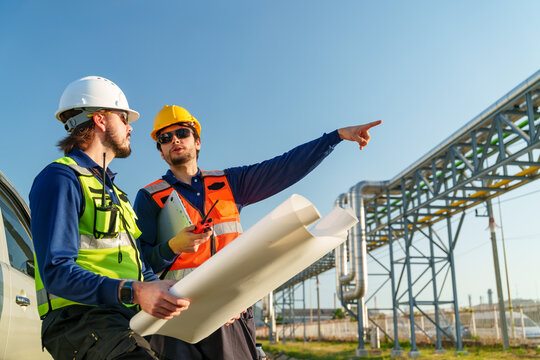 Two workers review blueprints at a construction site during the day with a clear sky