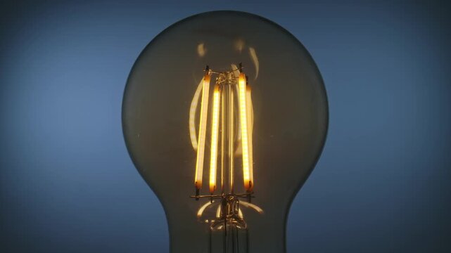 A detailed view of a stylish vintage filament light bulb glowing against a blue background, showcasing its design.