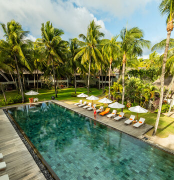 Aerial view of a serene pool reflecting the sky, surrounded by palm trees and lounge chairs in lush greenery, Prince Maurice, Flacq District, Mauritius.