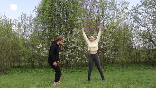 A young couple doing sports outdoors, gymnastics and physical education exercises with a rubber band