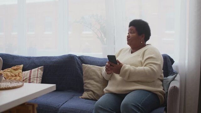 Medium shot of senior African American woman having problem with smartphone and asking her granddaughter for help