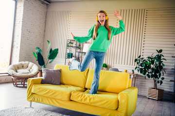 Naklejka premium Happy young woman enjoying leisure at home while standing on a vibrant sofa in a bright and stylish interior space