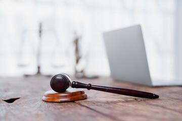 Gavel on a rustic wooden desk with a blurry scale of justice and laptop in the background,...